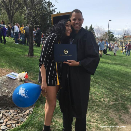Graduates posing outdoors with a diploma, surrounded by a grassy area and trees. 4